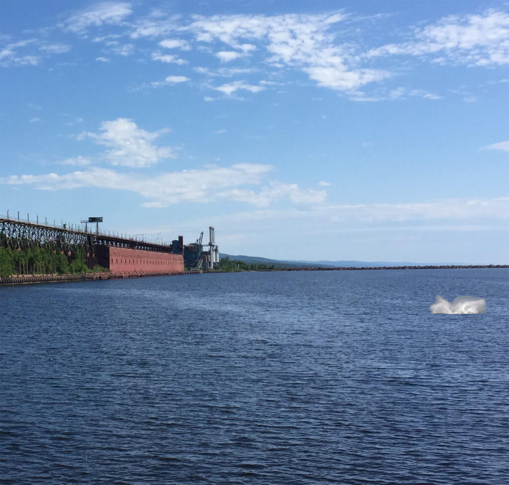 splash from a whale on lake superior with taconite harbor in the background